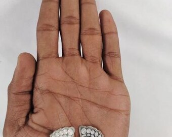 May include: Two silver foot-shaped pendants with intricate designs, including symbols and patterns. The pendants are displayed on a hand against a white background. The pendants are likely religious or spiritual items.