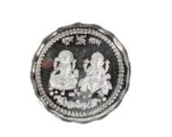 May include: A silver coin with a scalloped edge. The coin features two seated figures and text in a circular pattern. The figures are detailed with intricate designs. The coin is set against a white background.
