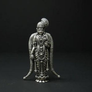 May include: A detailed silver statue of a deity, standing upright with ornate clothing and jewelry. The figure has a serene expression and is set against a dark background. The statue is approximately 6 inches tall.