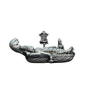 May include: A silver-colored sculpture depicting a reclining figure with intricate details. Two smaller figures are positioned near the main figure. The sculpture has a detailed base and is set against a white background.