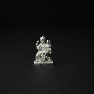 May include: A small, detailed silver statue of a deity, possibly Hindu, with multiple arms and ornate headdress. The statue is set against a stark black background, highlighting its intricate design and metallic sheen.