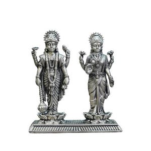 May include: Two silver-colored statues of Hindu deities. The statues are intricately detailed, with multiple arms and ornate headdresses. They stand on a decorative base, showcasing traditional religious artistry. The figures are depicted in a standing pose.