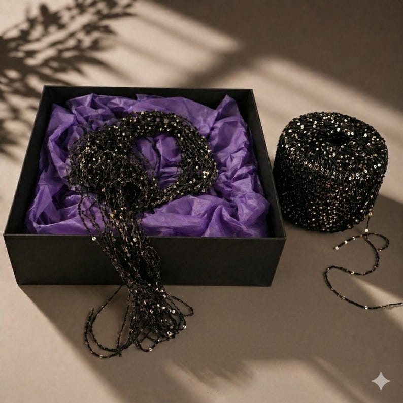 May include: A black box with a black beaded necklace and a spool of black beaded string. The box contains purple tissue paper. The beaded string is black with silver sequins.