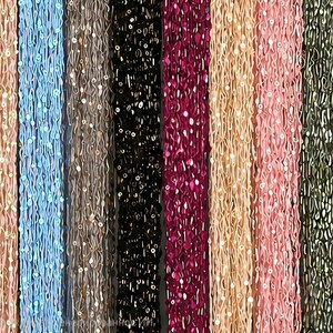May include: A collection of beaded strands in various colors, including pink, blue, black, and gold. Each strand is adorned with small, reflective sequins, creating a shimmering effect. The strands are arranged vertically, showcasing the diverse color palette.