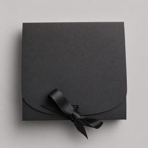 May include: A square, black gift box with a curved flap closure and a black satin ribbon tied in a bow. The box is made of a matte paper material and is closed with a black ribbon.