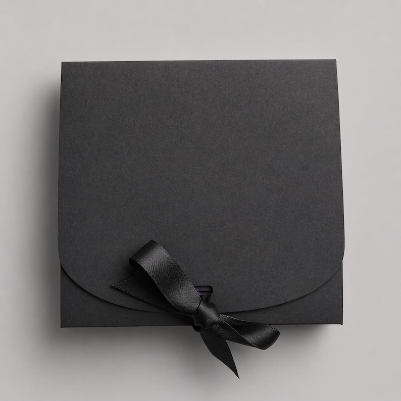 May include: A square, black gift box with a curved flap closure and a black satin ribbon tied in a bow. The box is made of a matte paper material and is closed with a black ribbon.