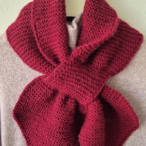 May include: A deep red knitted cowl neck scarf. The scarf is folded and displayed on a hanger.