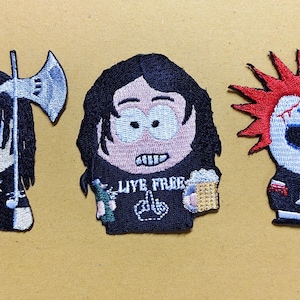 Puede incluir: Tres parches bordados con personajes de dibujos animados. El parche izquierdo muestra un personaje con pelo negro sosteniendo un hacha plateada. El parche central muestra un personaje con una camiseta negra con el texto LIVE FREE. El parche derecho muestra un personaje con pelo rojo puntiagudo y un símbolo anarquista blanco.