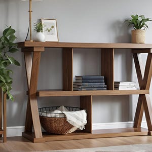 Może przedstawiać: Drewniany stolik konsolowy z naturalnym wykończeniem. Stół posiada otwarte półki i nogi w kształcie litery X. Książki, rośliny i kosz z kocem są eksponowane na półkach, tworząc stylowe rozwiązanie do przechowywania.