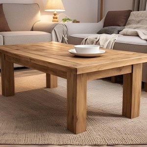 May include: A rectangular wooden coffee table with a natural wood finish. The table has a simple design with four legs and a wide top. The table is sitting on a woven rug.