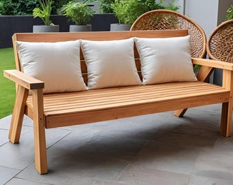 May include: A wooden bench with three white cushions. The bench has a slatted design and is made of natural wood. The bench is sitting on a patio.
