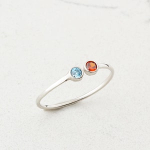 May include: A silver ring featuring a blue and orange gemstone. The ring is simple and elegant.
