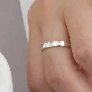 May include: A silver band ring with a delicate floral design engraved on the surface.