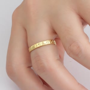 May include: A gold band ring with a textured surface and a design of small flowers and leaves.