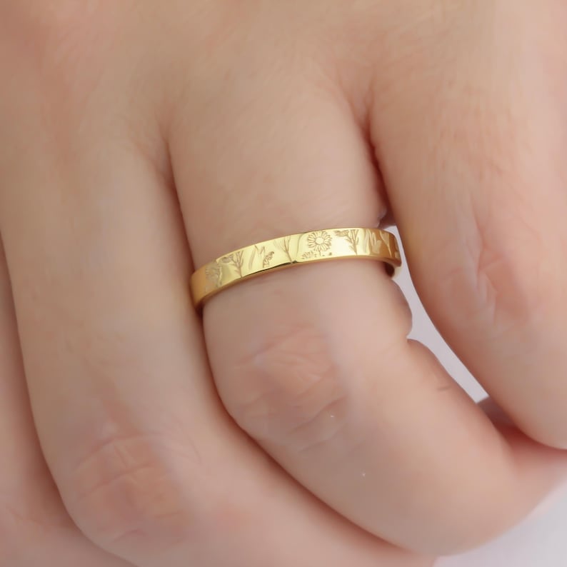 May include: A thin gold band ring with a delicate floral design engraved around the entire band.