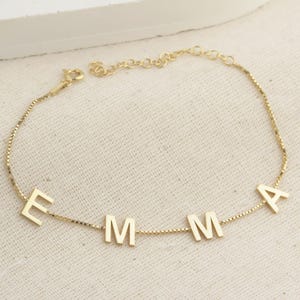 May include: A gold chain bracelet with the name "EMMA" spelled out in individual letters.