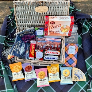 May include: A wicker basket filled with a variety of Scottish treats, including shortbread, fudge, and caramel. The basket is sitting on a plaid blanket.