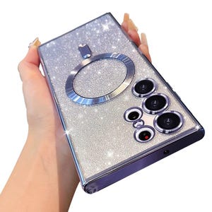May include: A silver glitter phone case with a ring holder and a camera lens cover. The case has a sparkly finish and a raised ring holder.