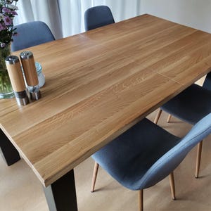 Puede incluir: Una mesa de comedor de madera con una base de metal negro y cuatro sillas azules. La mesa tiene un acabado de madera natural y una forma rectangular. Las sillas tienen un diseño moderno con un respaldo curvo y un asiento acolchado.