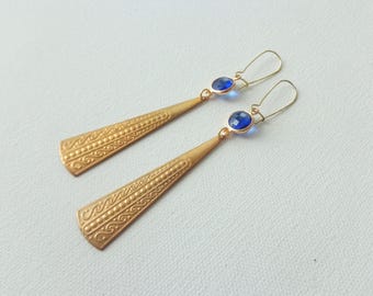 May include: A pair of gold dangle earrings with blue gemstone accents. The earrings feature a textured, geometric design.