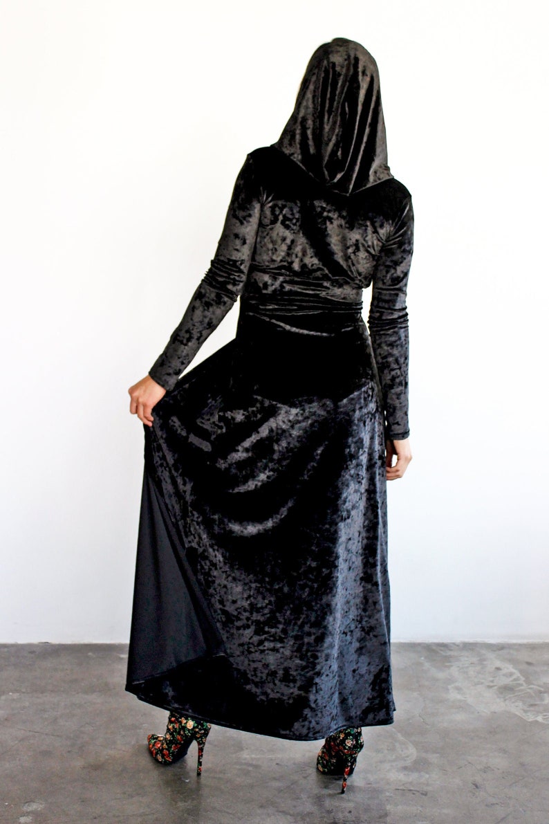 Peut inclure: Une robe maxi en velours noir &agrave; manches longues et &agrave; capuche. La robe a une texture froiss&eacute;e et une jupe ample.