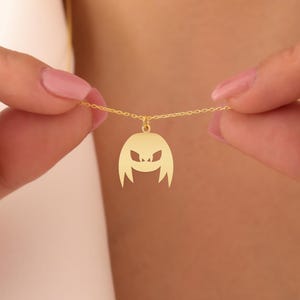 May include: A gold necklace with a pendant shaped like a cartoon character with a menacing expression.