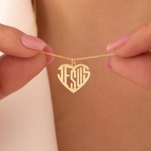May include: A gold necklace with a heart-shaped pendant that says "JESUS" in a monogram style.