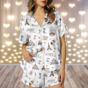 May include: White pajama set with a short-sleeved button-up shirt and shorts. The set features a repeating pattern of cartoon characters, the Eiffel Tower, and cooking-related imagery. The text "Gusteau's" is also visible on the pajamas.