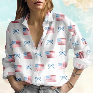 May include: White button-down shirt featuring a repeating pattern of watercolour American flags and blue bows. The long-sleeved shirt has a classic collar and is unbuttoned at the neckline.