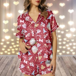 May include: Burgundy pyjama set featuring a whimsical pattern of teacups, bows, flowers, and magic wands. The short-sleeved top and shorts are trimmed with white piping. The fabric has a silky sheen.