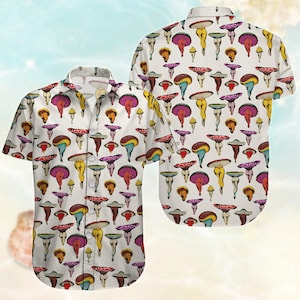 Puede incluir: Camisa blanca con botones con un patrón repetido de ilustraciones de hongos coloridos. Los hongos tienen varios colores de sombrero, incluyendo rojo, amarillo y morado, sobre un fondo blanco. La camisa tiene mangas cortas y un cuello clásico.