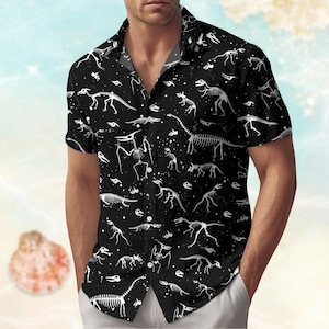Puede incluir: Camisa negra de manga corta con un estampado repetitivo de esqueletos de dinosaurios blancos. La camisa, con cuello clásico, presenta un diseño original con diferentes especies de dinosaurios. Fabricada en tejido ligero, ofrece un look único y atractivo.