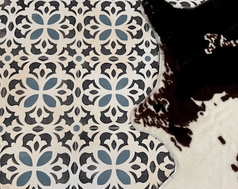 May include: Overhead shot of a patterned tile floor with a cowhide rug. The tile features a repeating floral design in white, black, and blue. The cowhide rug is black, brown, and white.