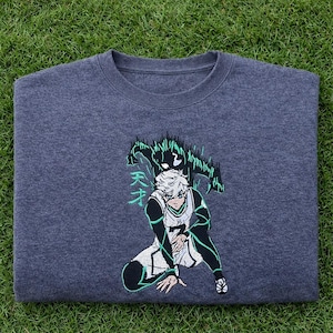 May include: Dark gray sweatshirt featuring an anime-style character in a basketball uniform. The design includes a green and black graphic above the character and Japanese text. The sweatshirt is displayed on a green grassy surface.