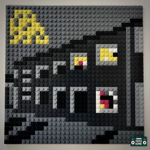 Puede incluir: Una obra de arte de mosaico cuadrado hecha de ladrillos de juguete grises, negros y amarillos. La obra de arte representa una cara estilizada con la palabra "ERROR" en letras blancas. Los ojos son amarillos y rojos. Una luna creciente amarilla está en la esquina superior izquierda.