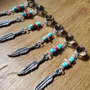 Op de afbeelding: Vijf zilverkleurige oorclips met veervormige hangers en turquoise en koraal kralen. De oorclips hebben een cirkelvormig ontwerp. De veren zijn gedetailleerd en de kralen zijn klein en rond.