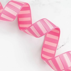 May include: A length of pink ribbon with alternating light pink and white stripes. The ribbon is curled and appears to be made of fabric. The background is a light, neutral color.