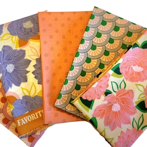 May include: A set of five fabric squares featuring different patterns. The patterns include a floral design with pink flowers and green leaves, a geometric pattern with orange, brown, and pink colors, a solid orange fabric, a geometric pattern with green and yellow colors, and a floral design with purple flowers and yellow accents. The fabric squares are arranged in a fan shape.