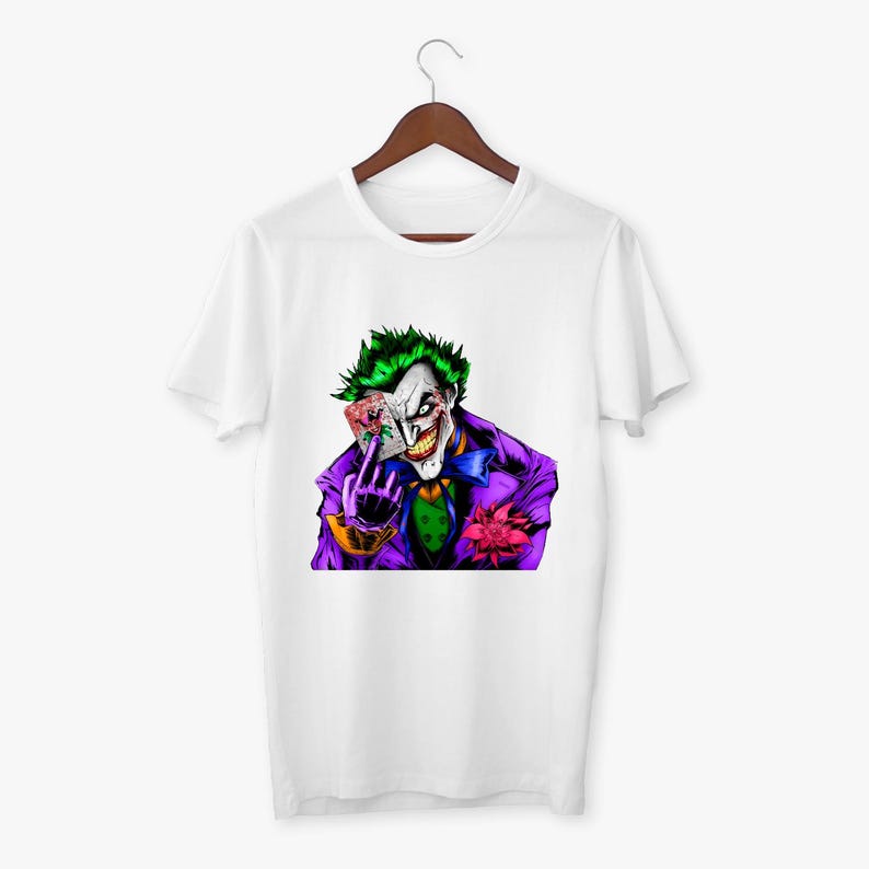 May include: White t-shirt featuring a colorful graphic of the Joker character. The Joker is depicted with green hair, white face paint, and a purple suit, holding playing cards. A pink flower is pinned to his lapel.