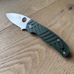 May include: A green pocket knife with a silver blade and a textured handle. The knife has a small hole in the blade for opening it.