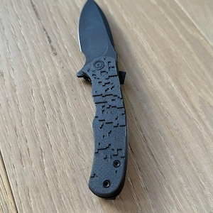 May include: A black folding knife with a textured handle and a partially visible blade.