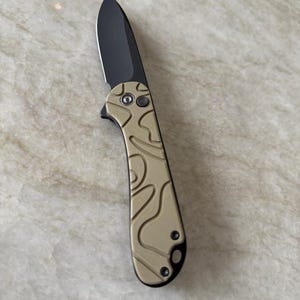 May include: A black folding knife with a tan camouflage pattern handle.