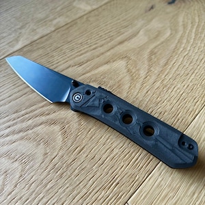 May include: A black folding knife with a black handle and a silver blade. The handle has a textured pattern and several holes.