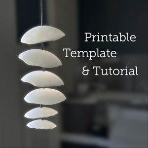 May include: A printable template and tutorial for making a mobile with six white, round, paper shapes hanging from a string.