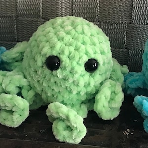 May include: Three crocheted octopus plushies in blue, green, and light blue. Each octopus has large black eyes and eight tentacles.