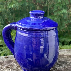 Könnte beinhalten: Eine blaue Keramikdose mit Deckel und Henkel. Die Dose ist glasiert und hat eine glänzende Oberfläche.