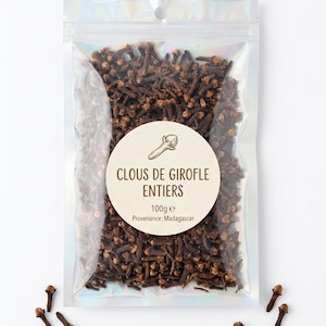 May include: A clear, resealable pouch filled with dark brown whole cloves. A circular white label on the front features a line drawing of a clove, the text CLOUS DE GIROFLE ENTIERS, 100g e, and Provenance: Madagascar. Several loose cloves lie nearby.