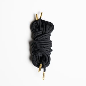 May include: A pair of black shoelaces with gold aglets. The laces are tied together in a knot.
