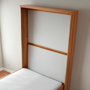 Peut inclure: Un lit mural en bois avec un matelas blanc. Le lit est repli&eacute; et semble &ecirc;tre dans un placard.