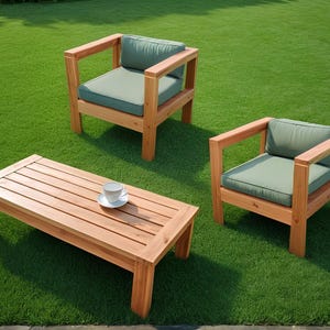 May include: Wooden garden furniture set comprising a rectangular coffee table and two armchairs with green cushions. A white teacup and saucer are on the table, set on green grass.
